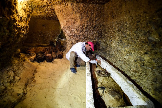 Một nhà khảo cổ đang xem xét xác ướp được đặt trong quan tài bằng đá.