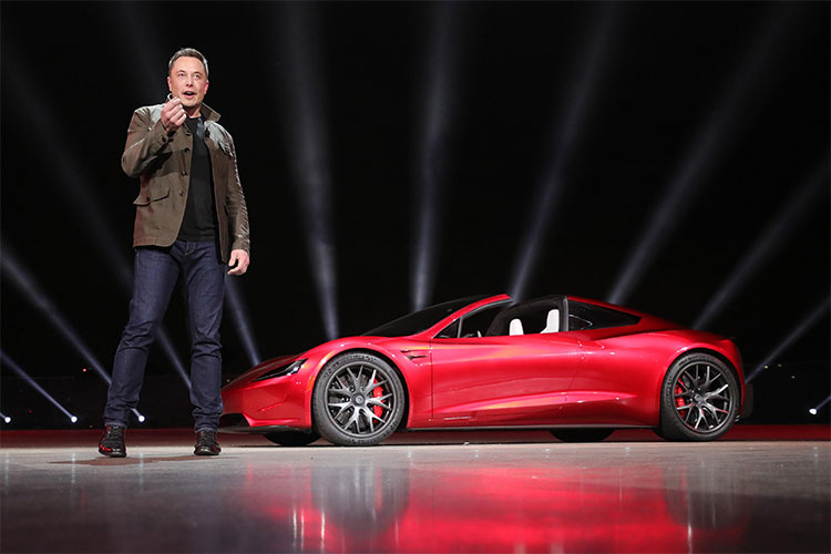 Tỷ phú Elon Musk, CEO SpaceX, đứng bên cạnh chiếc xe điện Tesla Roadster mui trần màu đỏ.